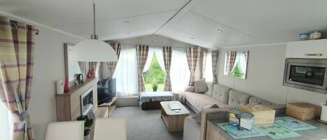 A compact RV interior with a kitchenette, a dining area, a sofa, and a TV.