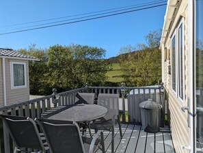 Una terraza con mesa y sillas, un cubo de basura y vistas a un paisaje verde.