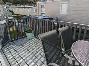 A deck with a table and chairs, a potted plant, and a view of mobile homes. - Clarach Bay Holiday Village W18 (Aberystwyth)