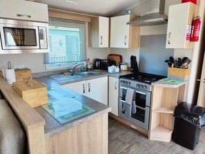 Een kleine keuken met een magnetron, fornuis, oven, spoelbak en houten kastjes.