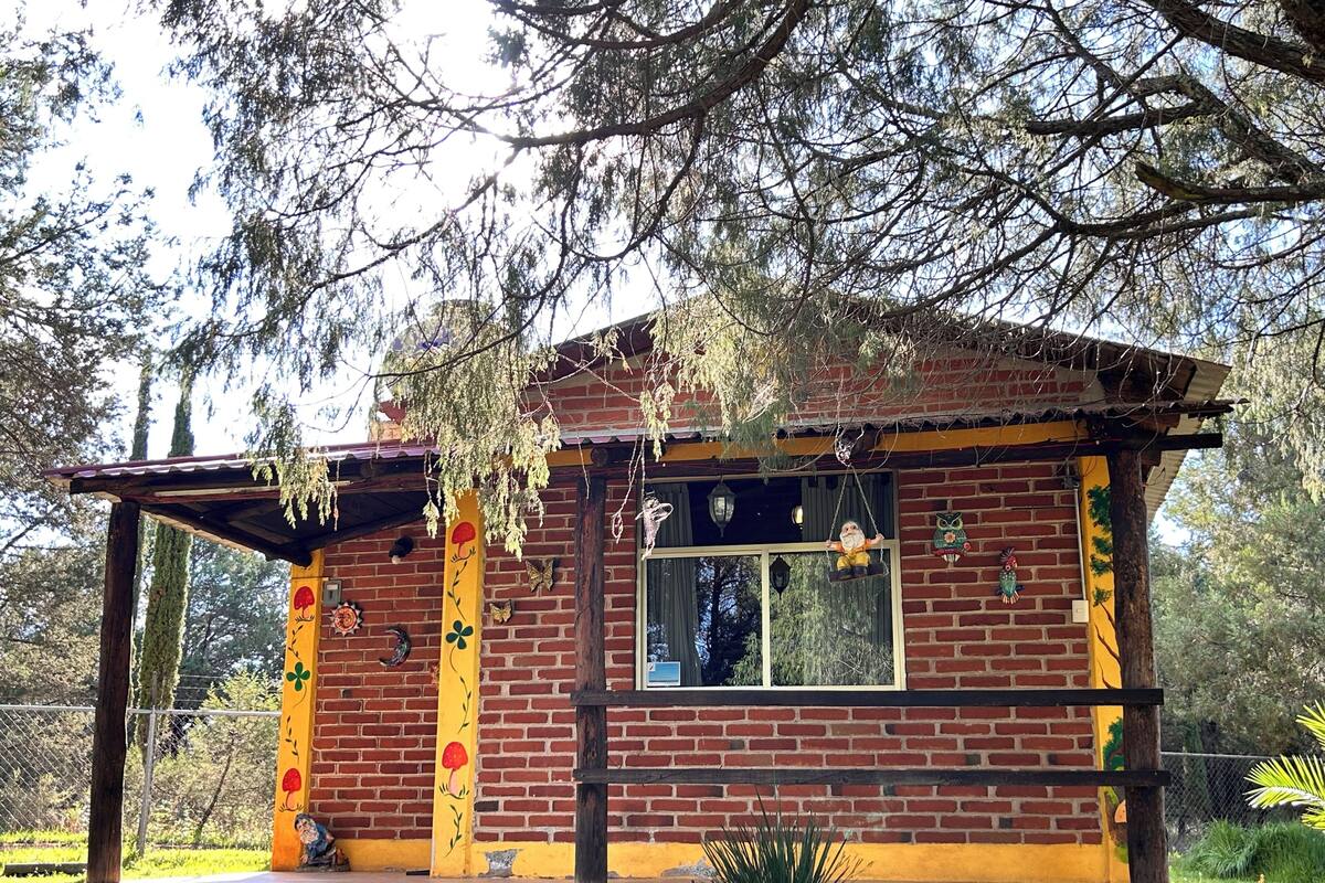 A small brick building with a porch, a window, and decorative elements like a gnome and a birdhouse.