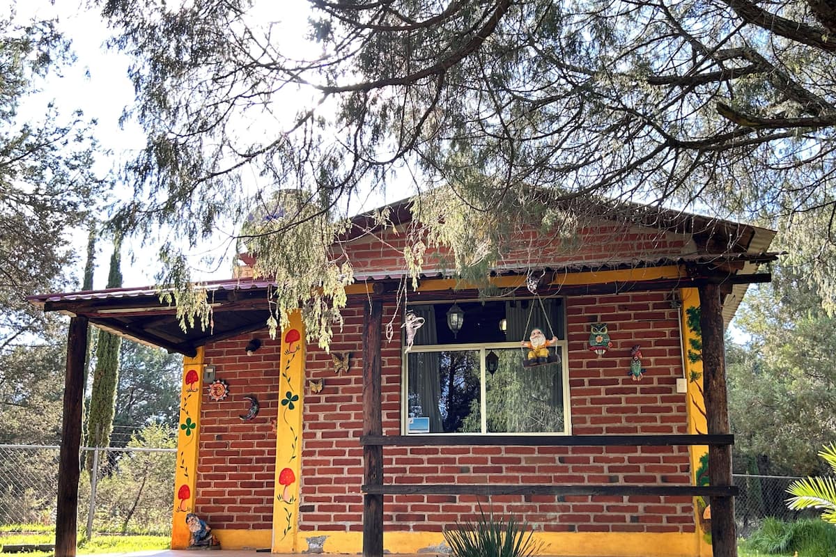A small brick building with a porch, a window, and decorative elements like a gnome and an owl.