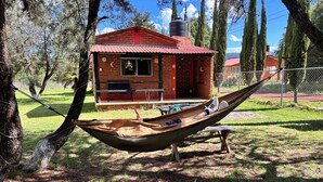 Un'amaca legata tra due alberi, una casetta in mattoni con tetto rosso e un patio in pietra.