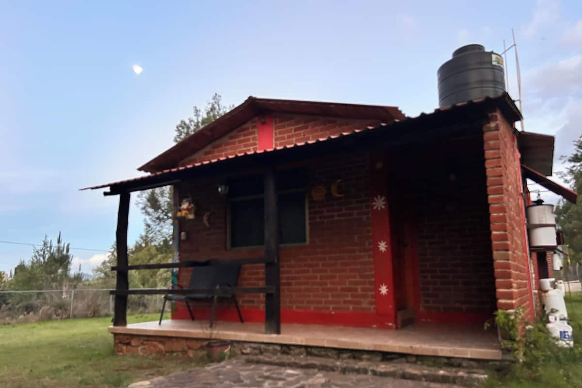 A small brick building with a red roof, a porch with a chair, and a water tank on the roof.