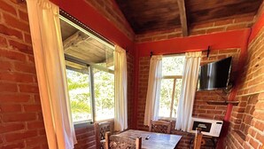 Zona pranzo con parete in mattoni, tavolo di legno, sedie e finestra con tende.
