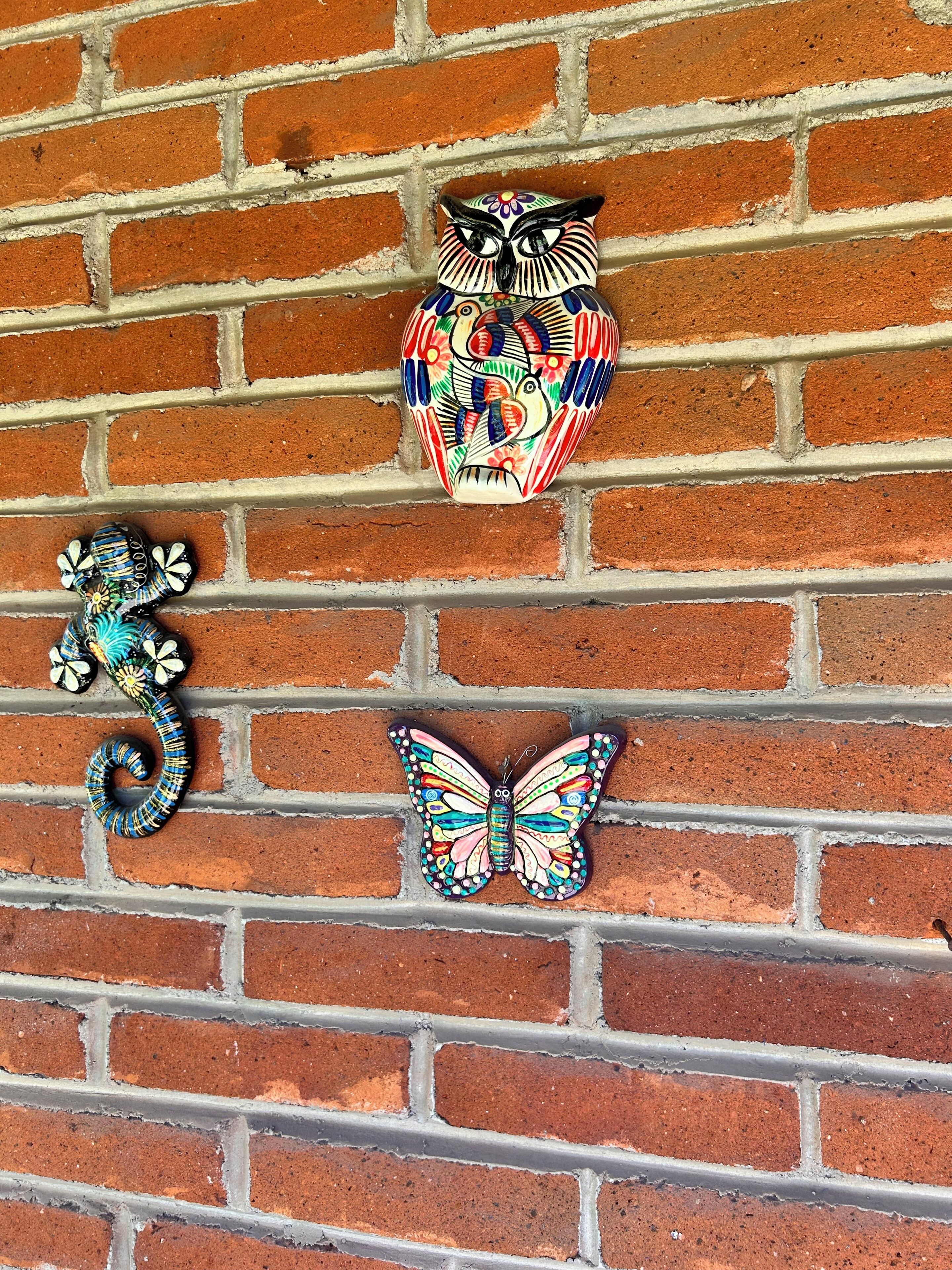 Un mur de briques orné de trois éléments décoratifs : une chouette, un papillon et un hippocampe.