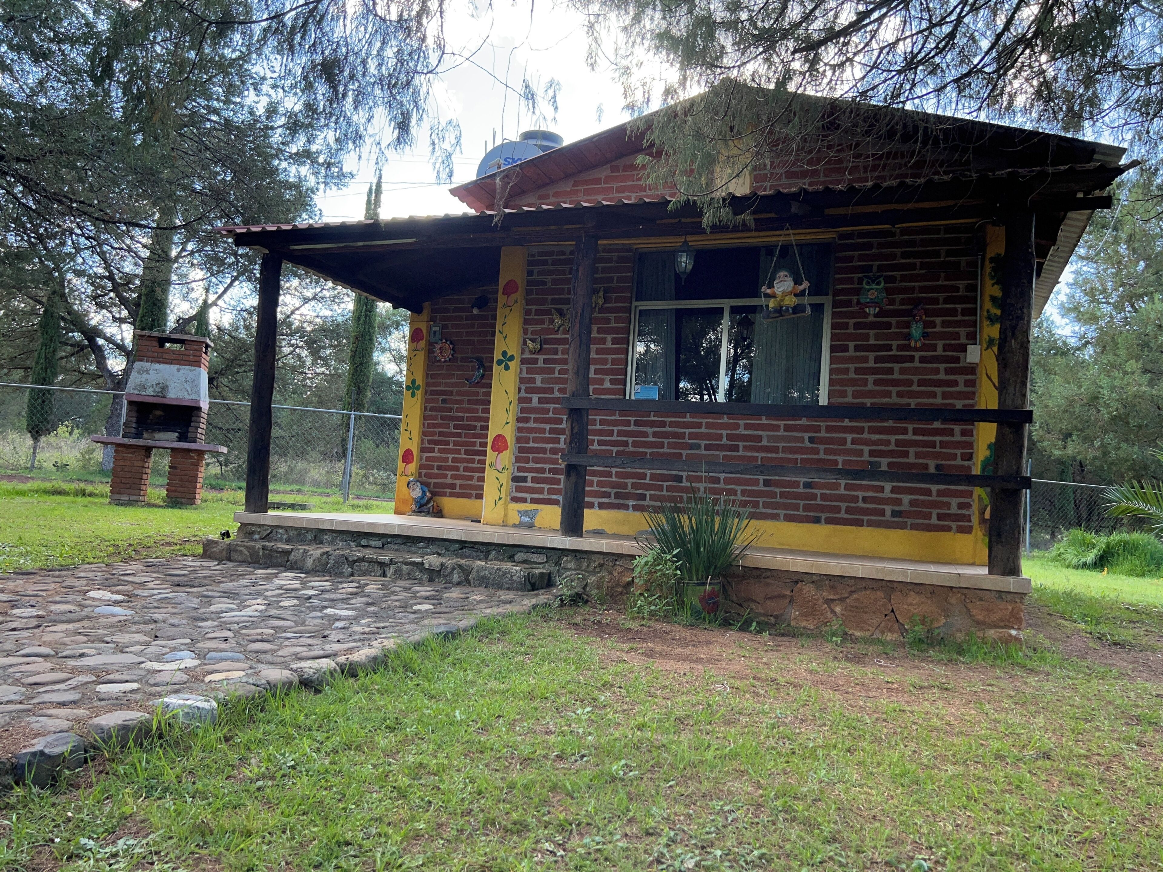 Un edificio de ladrillo con un pequeño porche, un camino de piedra y un área cercada con árboles.