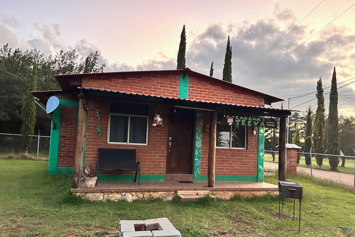 A small brick house with a porch, a satellite dish, and a sign that reads 'CABANA TREVA.'