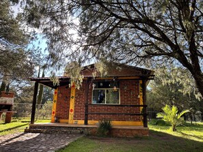 A small brick building with a porch, surrounded by trees and grass.