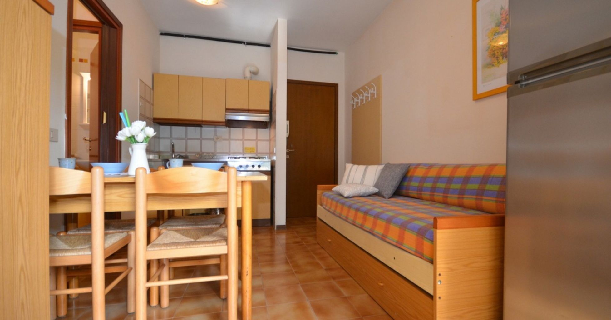 A compact living space with a kitchenette, a wooden dining table with chairs, and a colorful sofa.