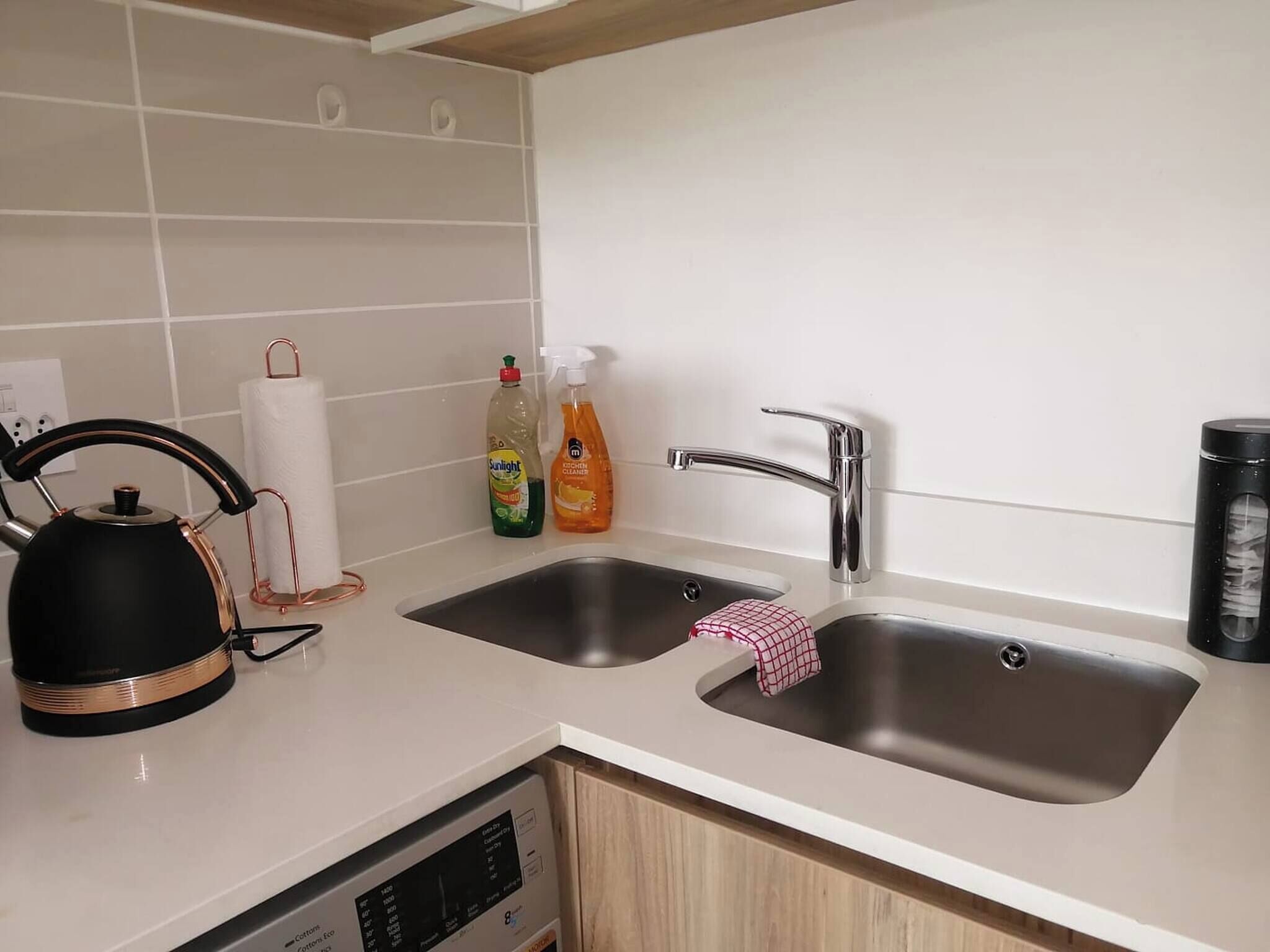 A kitchen with two sinks, a kettle, a dish soap bottle, a dish soap pump bottle, a dish towel, and a coffee maker.