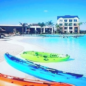 A beach resort with a pool, kayaks, and a building with multiple floors.