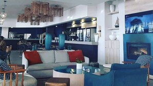 A modern living room with a sofa, coffee table, and chairs, a kitchen area with bar counters, and a fireplace. - The Blyde Modern Oasis Pretoria (Pretoria)