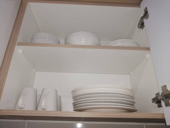 A cabinet with three shelves, each holding white plates and cups.