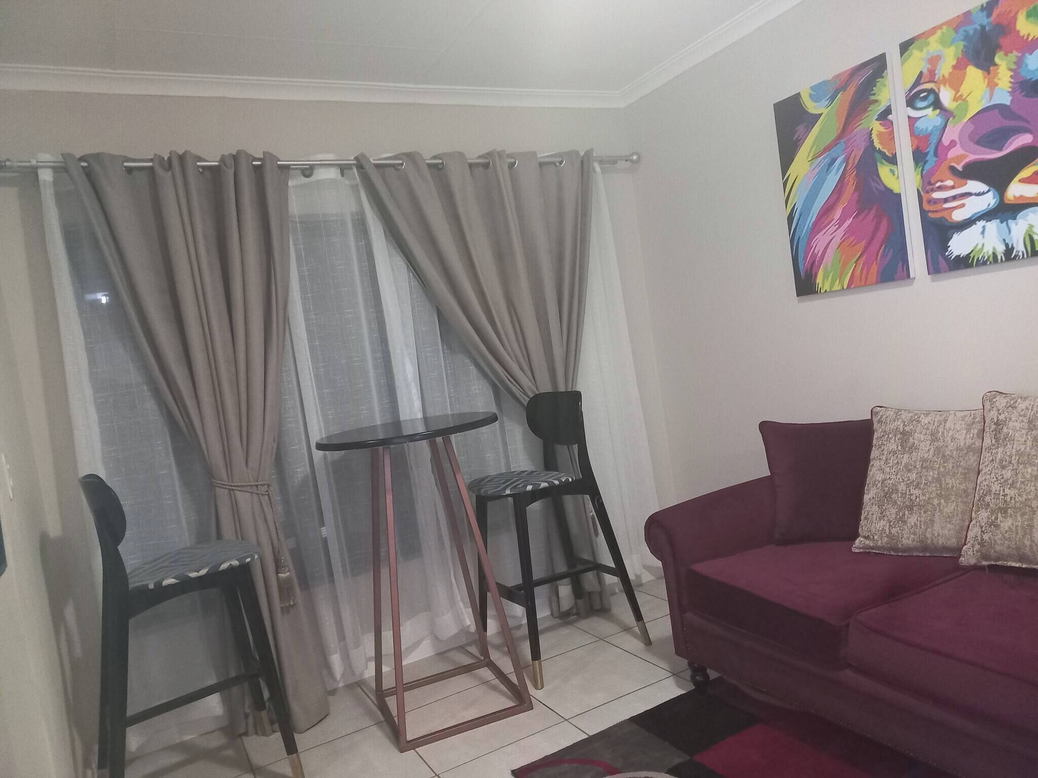 A living room with a red sofa, two chairs, a small round table, and a window with curtains.