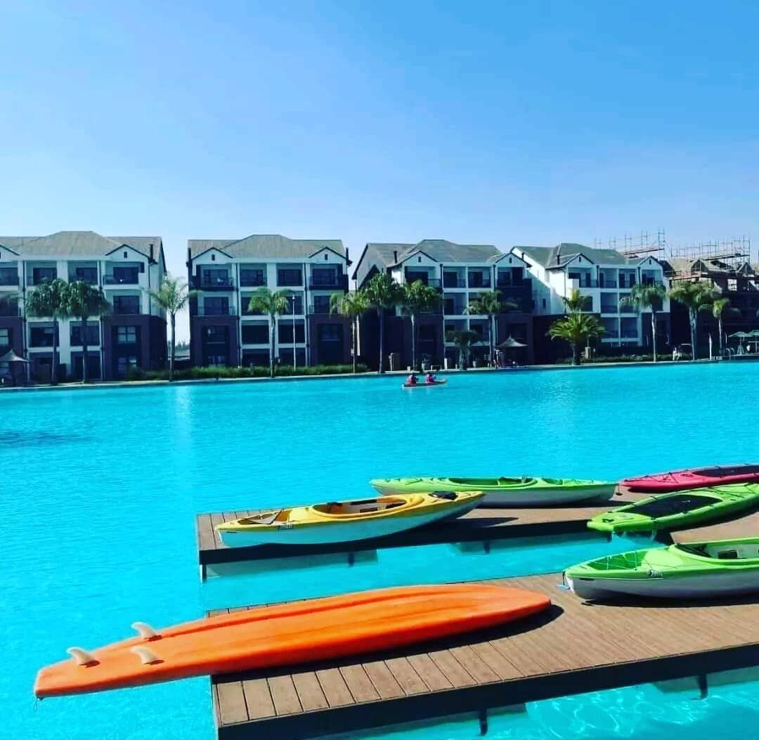 Una piscina con kayaks y una tabla de paddle surf, rodeada de edificios de varios pisos con balcones y palmeras.