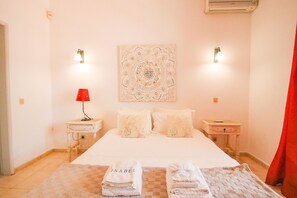 Habitación de hotel con cama, dos mesitas de noche, lámpara roja, tapiz en la pared y toallas en el suelo.