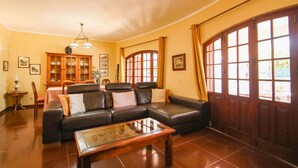 A living room with a leather sofa, a glass coffee table, a wooden cabinet, and a dining area with a table and chairs. - Villa with heatable pool and BBQ in Carvoeiro (Carvoeiro)