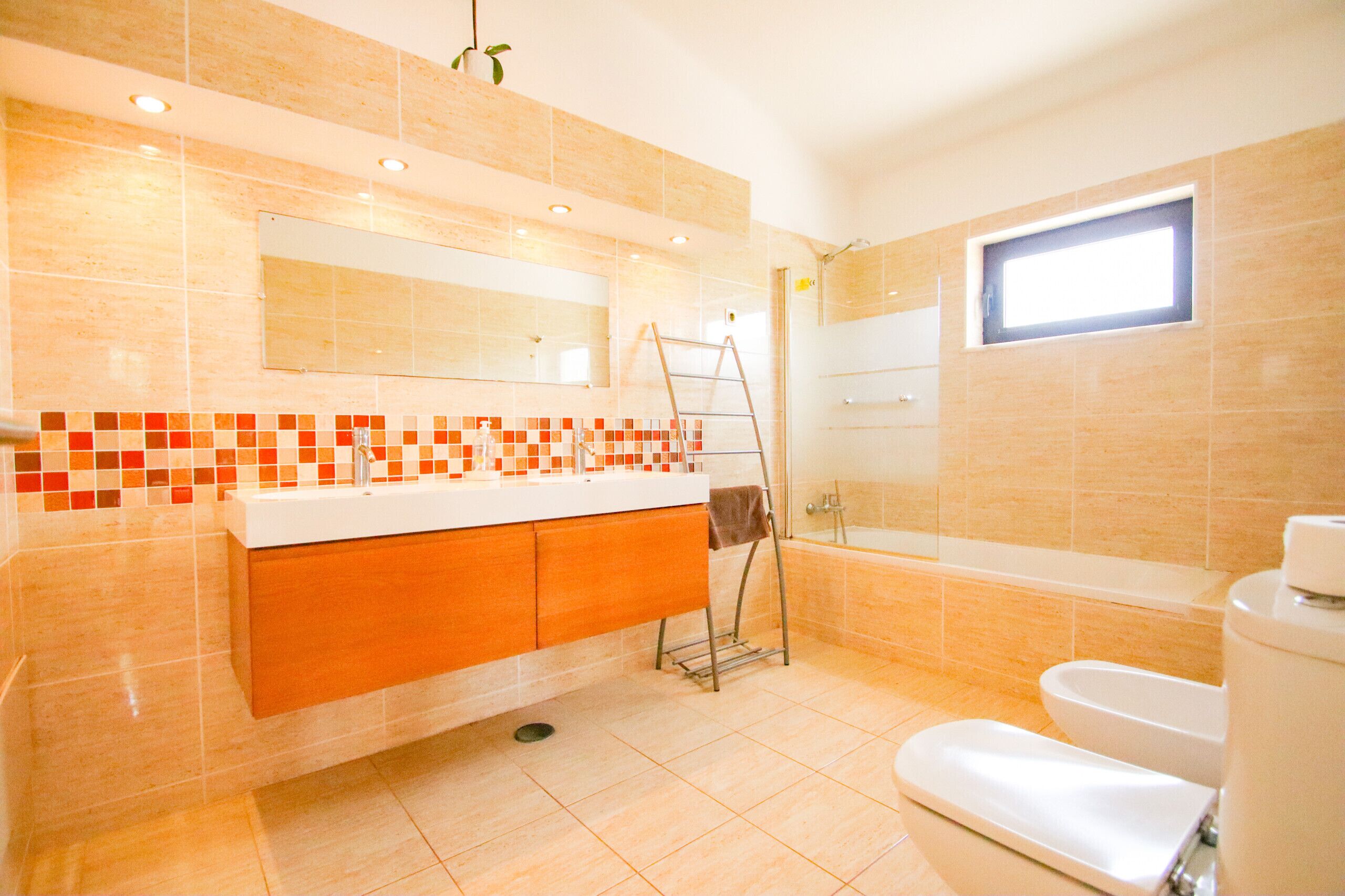 Une salle de bain équipée d’une baignoire, de toilettes et d’un lavabo, avec un mur recouvert de carreaux et une fenêtre.