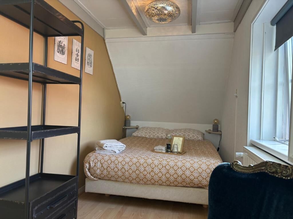 A bedroom with a bunk bed, a bedside table, a lamp, a window, and a bed with a patterned bedspread.