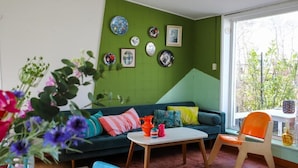 Um quarto com parede verde, sofá azul, mesa branca e janela com vista para vegetação.
