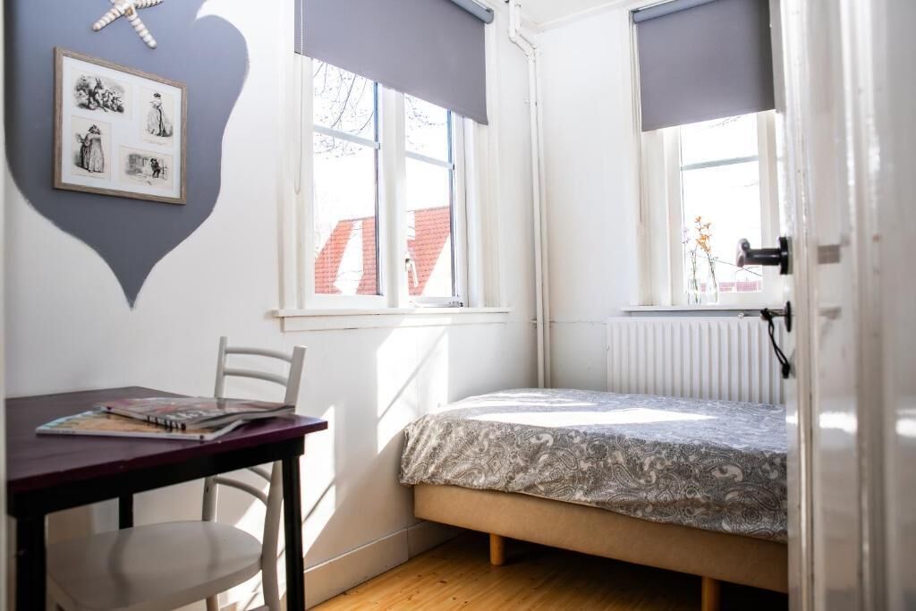 A small bedroom with a bed, a desk, and a chair. There is a window with a view of a building outside.