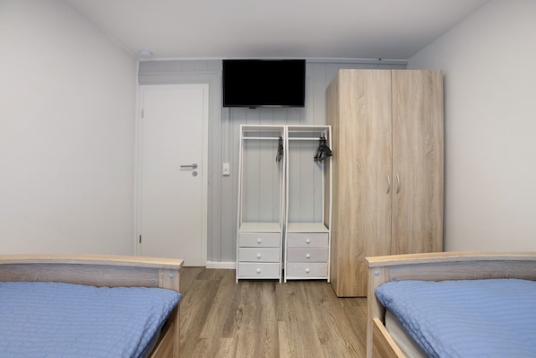 A bedroom with two beds, a wardrobe, a TV, and a door.