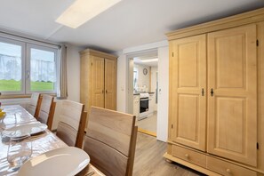 Un coin repas avec une table dressée pour six personnes, des chaises en bois et une vue par la fenêtre.