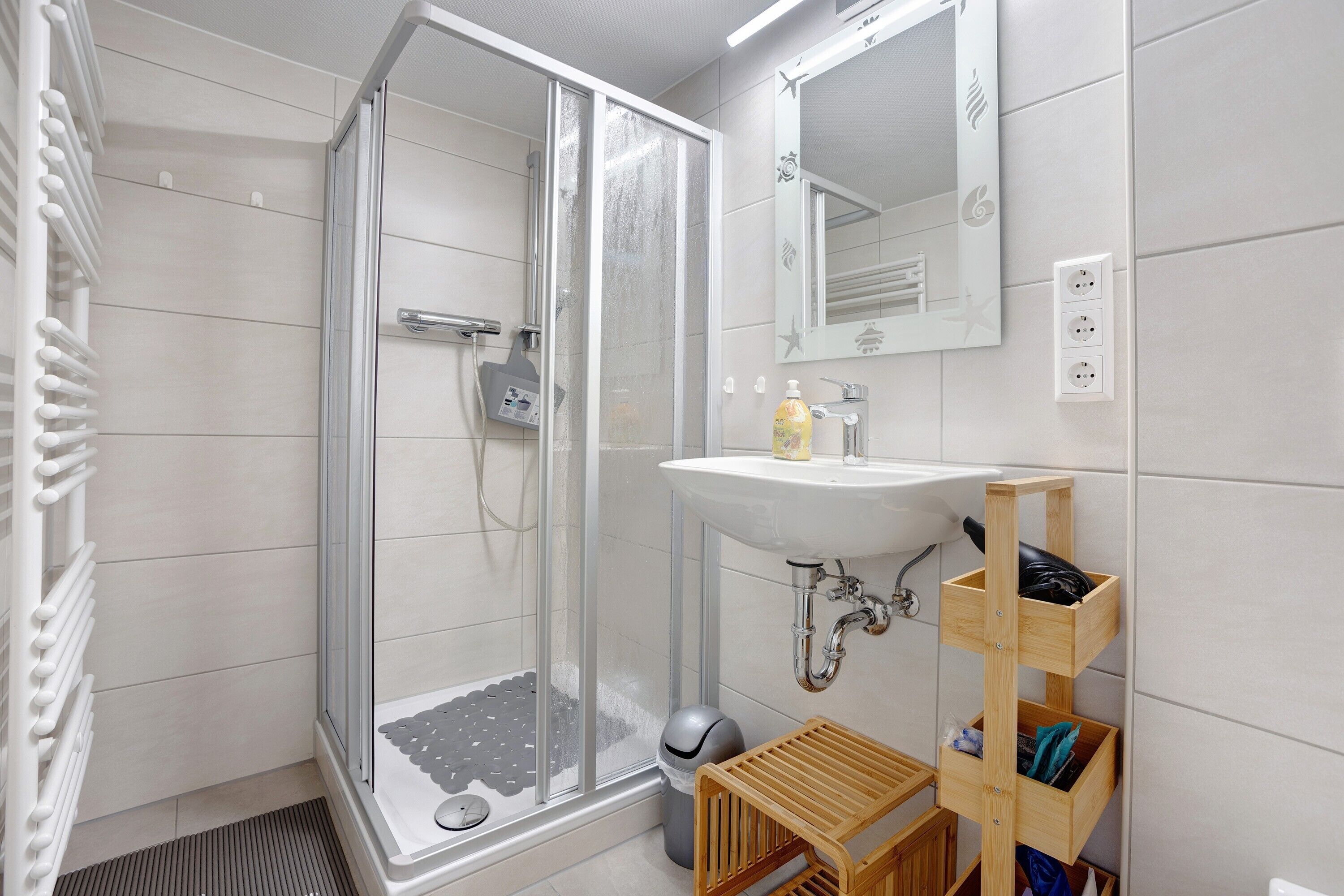 Un baño moderno con cabina de ducha de vidrio, un lavabo con repisa de madera y un espejo.