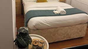 A neatly made bed with a green throw, a small plant, and rolled towels on a tray.