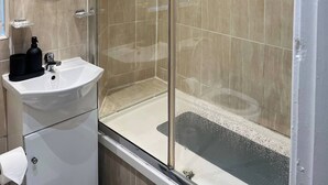 A modern bathroom with a glass-enclosed shower, a white sink, and a round mirror.