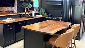 A modern kitchen with a central island, black cabinetry, wooden countertop, and stainless steel appliances. - Luxurious Smoky Mountain Getaway Hot Tub 💦 Pool Sauna & Fishing 🐠 EV Charge ⚡️ (Sevierville)