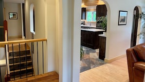 A modern interior with a staircase, wooden flooring, and a kitchen area with dark cabinetry and a window. - Cozy Mountain Retreat | Steps to Bow River (Canmore)