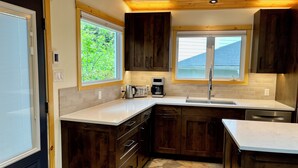 A modern kitchen with dark wooden cabinets, a white countertop, a built-in sink, and a window providing natural light. - Cozy Mountain Retreat | Steps to Bow River (Canmore)