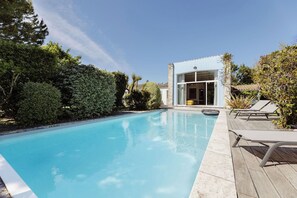 Un área de piscina moderna con una piscina azul cristalina, sillas de descanso y un edificio con grandes ventanales.