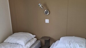 Een kamer met twee eenpersoonsbedden, een houten kast erboven, een wandlamp en een klein nachtkastje.