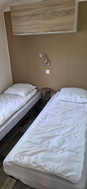 A room with two single beds, a wooden cabinet above, a wall-mounted light, and a small bedside table. - 🌴 Air-conditioned 3-bedroom mobile home - Camping 4★ - Île d'Oléron 🌴 (Dolus-d'Oléron)