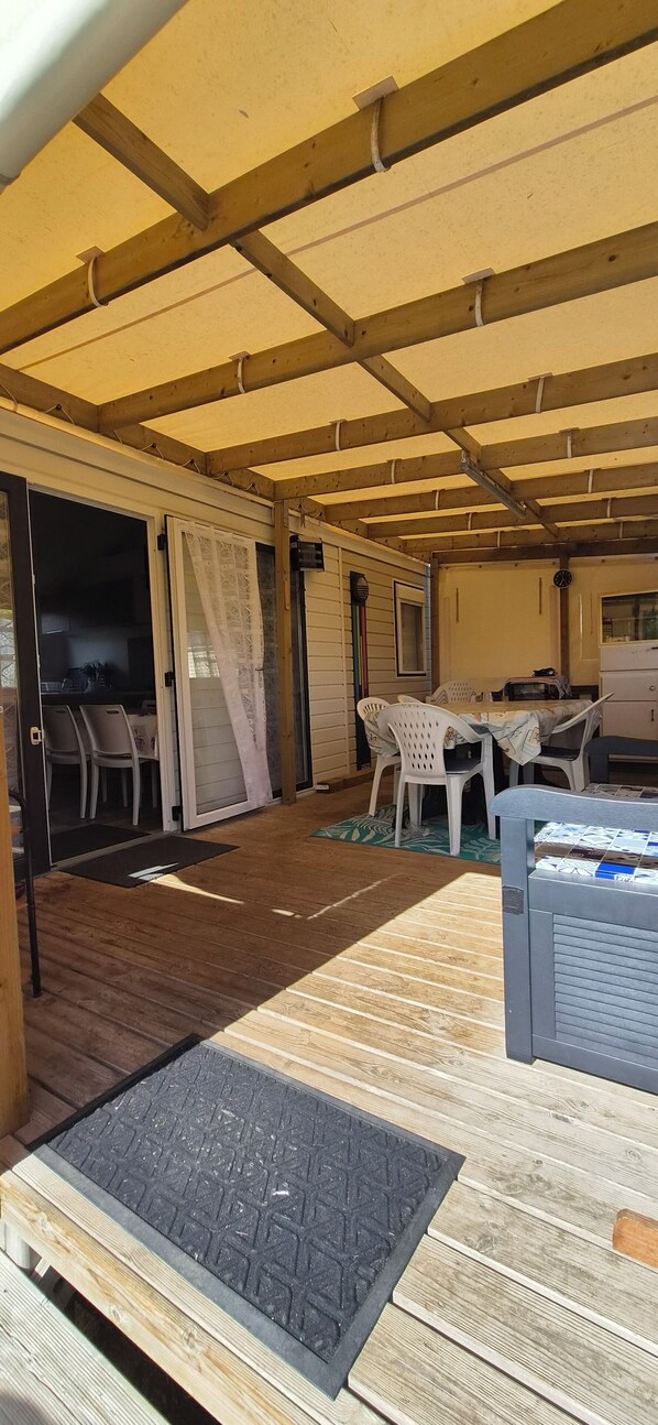 A covered outdoor area with a wooden floor, a table with chairs, and a refrigerator. - 🌴 Air-conditioned 3-bedroom mobile home - Camping 4★ - Île d'Oléron 🌴 (Dolus-d'Oléron)