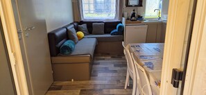 A compact living space with a sofa, a small kitchen area, and a dining table. - 🌴 Air-conditioned 3-bedroom mobile home - Camping 4★ - Île d'Oléron 🌴 (Dolus-d'Oléron)