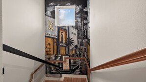 A staircase with a handrail, a wall with a mural of a cityscape, and a framed picture of a menu. - Sleep In Style Fashion House W/Pool Table Sleep 10 (Houston)