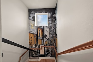 Eine Treppe mit Handlauf, eine Wand mit einem Stadtbild-Fresko und ein gerahmtes Bild eines Speisekarten.