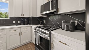 A modern kitchen with white cabinetry, a black stove, a microwave, and a coffee maker. - Sleep In Style Fashion House W/Pool Table Sleep 10 (Houston)