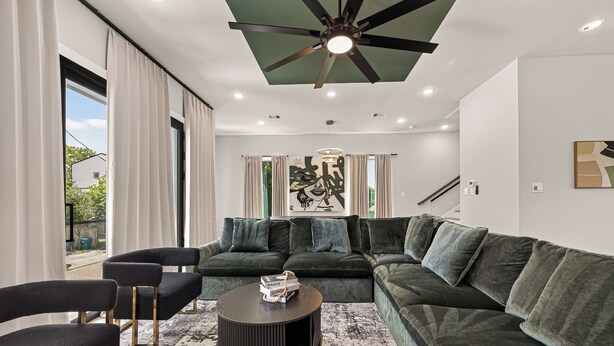 A modern living room with a sectional sofa, a coffee table, and a ceiling fan. - Sleep In Style Fashion House W/Pool Table Sleep 10 (Houston)