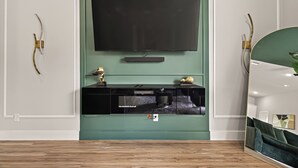 A modern living room with a large flat-screen TV mounted on a green wall, a black entertainment unit below, and a wooden floor. - Sleep In Style Fashion House W/Pool Table Sleep 10 (Houston)