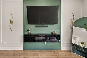 Ein modernes Wohnzimmer mit einem großen Flachbildfernseher an einer grünen Wand, einer schwarzen Unterhaltungseinheit darunter und einem Holzboden.