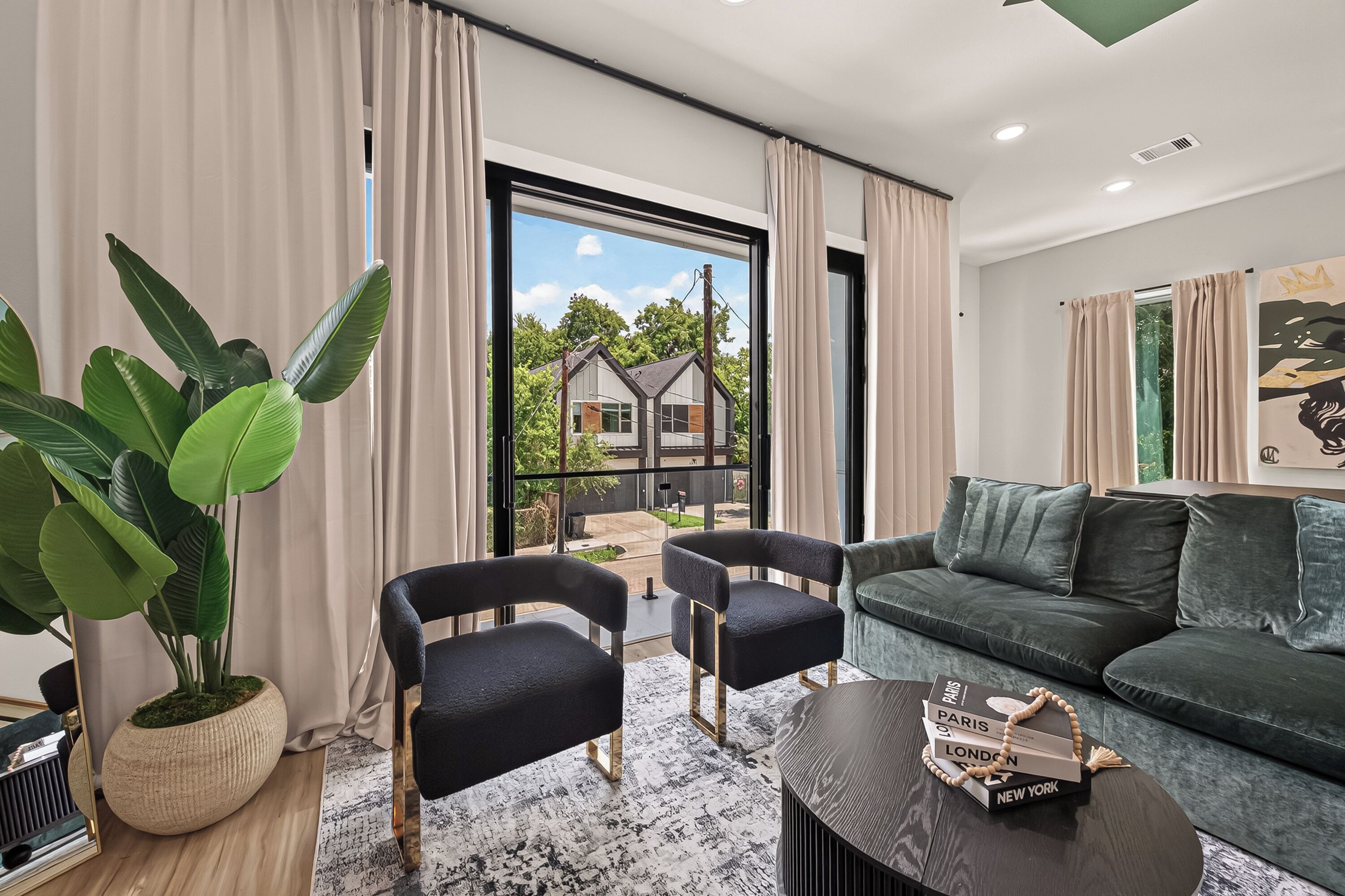 A modern living room with a sofa, two armchairs, a coffee table, and a large potted plant.