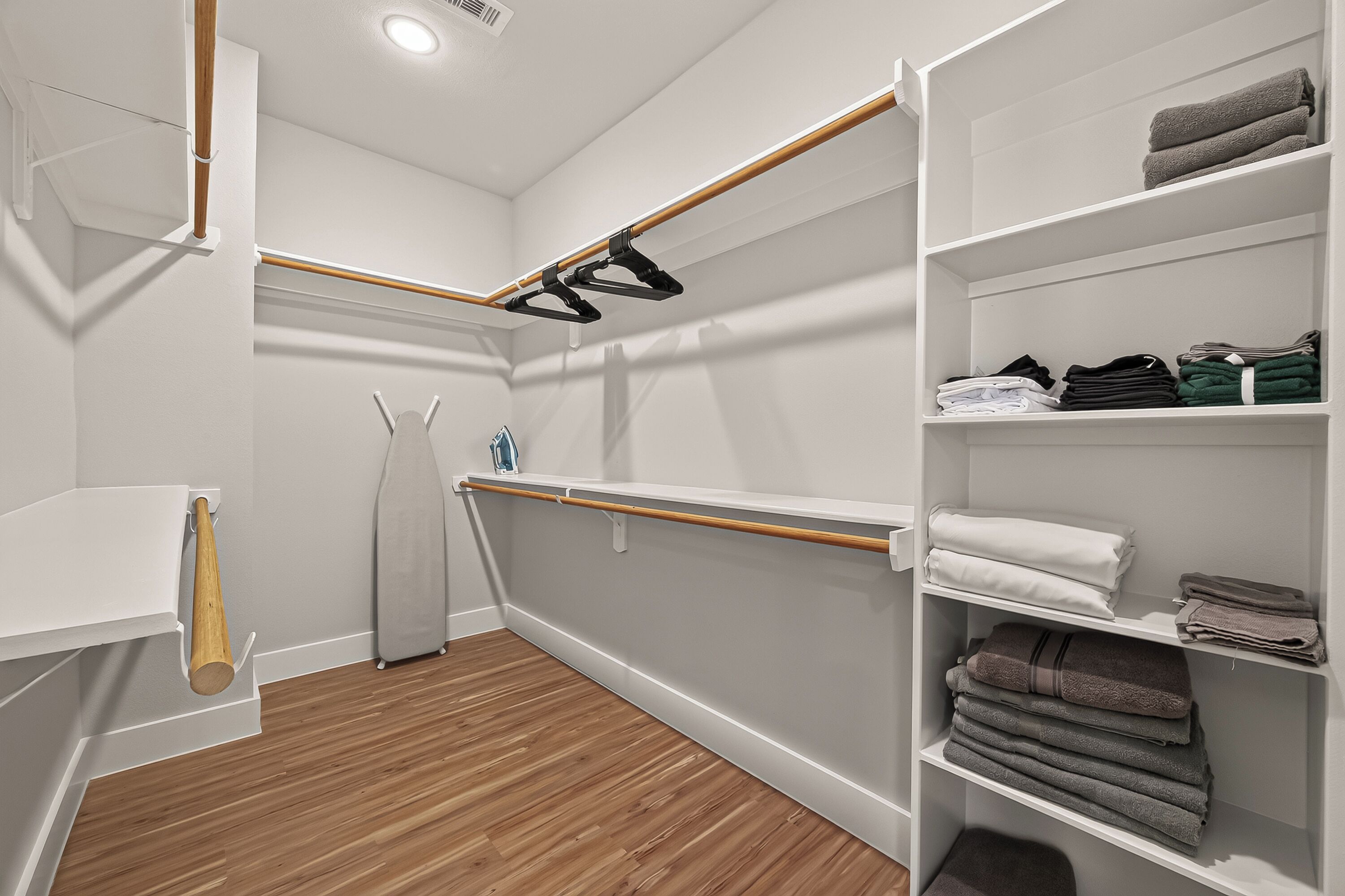 Un baño moderno con suelo de madera, paredes blancas y un estante empotrado con toallas dobladas.