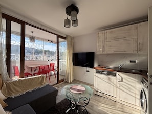 Un appartement moderne doté d’un balcon, d’un coin repas, d’une cuisine avec machine à laver et d’un téléviseur.