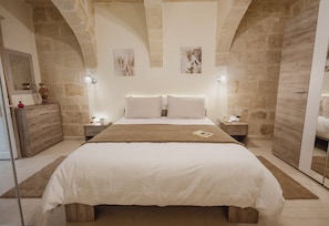Ein Schlafzimmer mit einem großen Bett, zwei Nachttischen, einem Beistelltisch, einem Spiegel und Steinwänden.