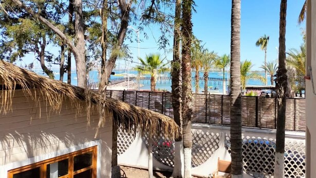 Una cabaña junto a la playa con techo de paja, puerta de madera y una ventana.